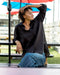 Person wearing a black shirt and blue jeans sitting outdoors under a blue umbrella.