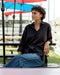 Person wearing a black shirt and blue jeans sitting outdoors under a blue umbrella.