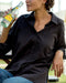 Person wearing a black shirt and blue jeans sitting outdoors under a blue umbrella.