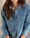 A woman wearing a long-sleeved, blue chambray utility shirt with button-up front and chest pockets.