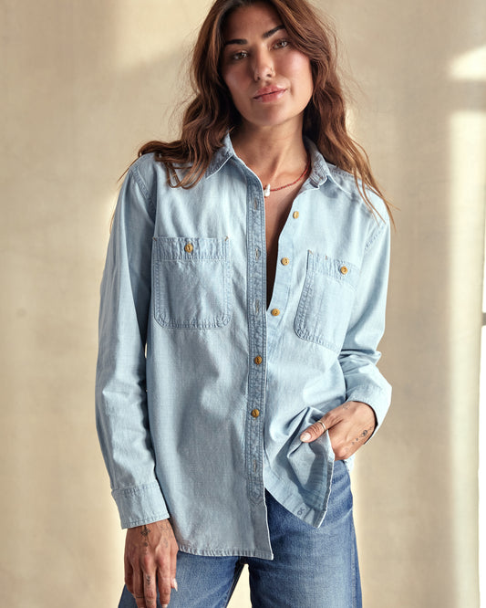 A woman wearing a blue chambray utility shirt with chest pockets and button closure, paired with high-waisted blue jeans.