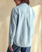 Closeup of the back of a woman wearing a blue chambray utility shirt with chest pockets and button closure, paired with high-waisted blue jeans.