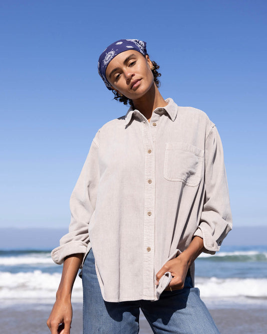 Person wearing a beige shirt and blue jeans on a beach with a clear blue sky.
