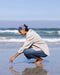 Person crouching on a beach, looking at something in the sand.