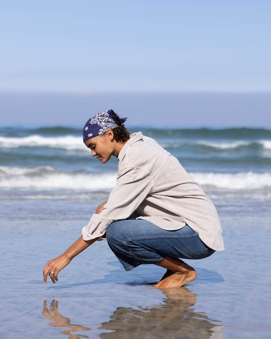 Person crouching on a beach, looking at something in the sand.