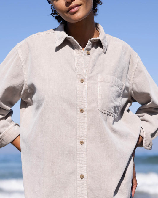 Person wearing a light beige button-up shirt with a blurred beach background