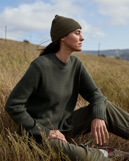 Woman sitting in a field wearing a green sweater and beanie