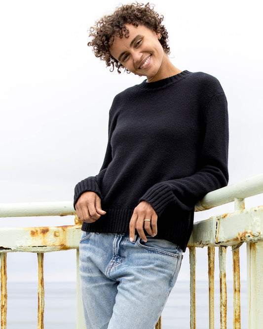 Person wearing a black sweater and light blue jeans standing on a rusty metal railing.
