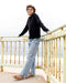 Person wearing a black sweater and light blue jeans standing on a rusted metal platform by the sea.
