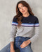 A woman wearing a striped sweater with a crew neckline, where the stripes feature shades of gray, blue, and purple, and the brand logo 'OK' is visible on the chest.