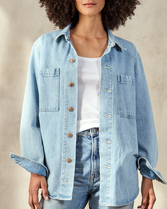 A woman wearing an oversized blue denim shacket with button-down cuffs and chest patch pockets, paired with a white top and blue jeans.