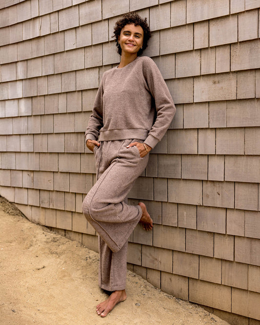 Person wearing a beige tracksuit leaning against a wooden wall.