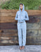 Person wearing a light blue hoodie and pants standing against a wooden wall.