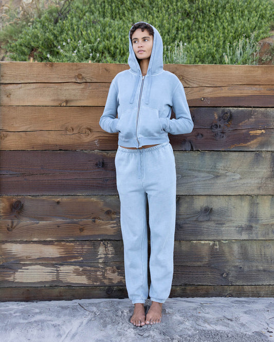 Person wearing a light blue hoodie and pants standing against a wooden wall.