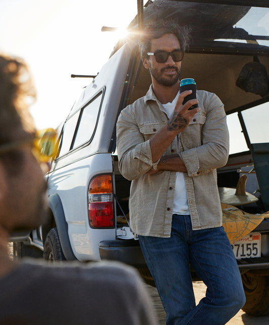 Man wearing a long-sleeved, button-up, beige utilitarian shirt with chest pockets.