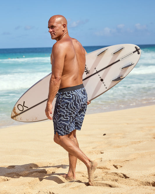 Kelly Slater wearing boardshorts with a geometric pattern in shades of blue and light blue, featuring a drawstring waistband.
