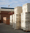 Stacks of white bales with visible text on a concrete ground with a building in the background.