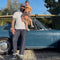 Man holding two children in front of a vintage car with palm trees and greenery in the background