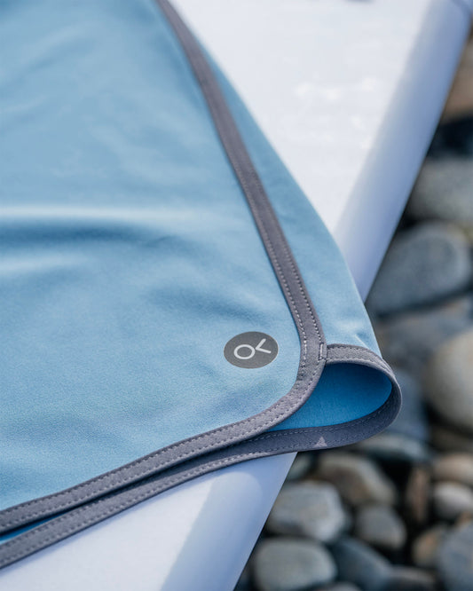 Close-up of a blue fabric with a gray zipper and logo, placed on a white surface with a stone background.