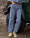 Person wearing blue pants and beige boots standing next to a green jeep.