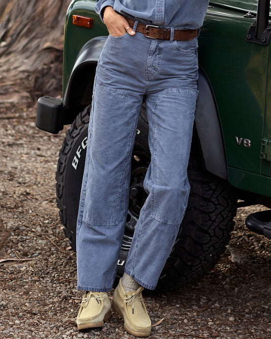 Person wearing blue pants and beige boots standing next to a green jeep.