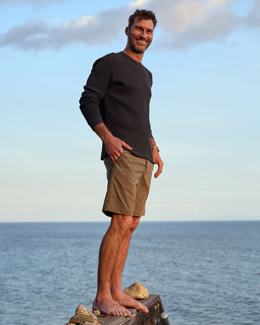 Man standing on a rock by the ocean with a clear sky