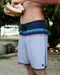 Person wearing striped board shorts holding a coconut outdoors