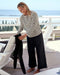 Woman in a striped shirt and wide-leg pants standing on a deck with ocean view