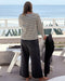 Person wearing a striped shirt and dark pants standing on a deck with ocean view