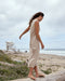 Woman in a beige dress standing on a beach with ocean and sky in the background