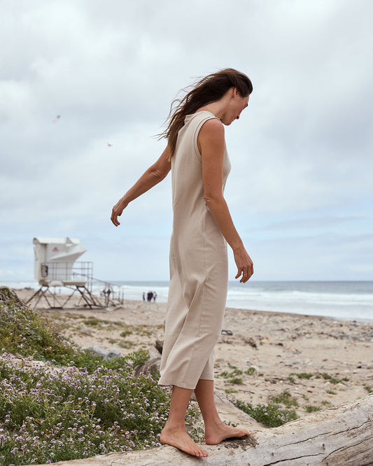 Woman in a beige dress standing on a beach with ocean and sky in the background