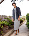 Woman in a striped dress and denim jacket walking along a garden path.