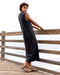 Woman in a black sleeveless dress standing on a wooden dock with a white background