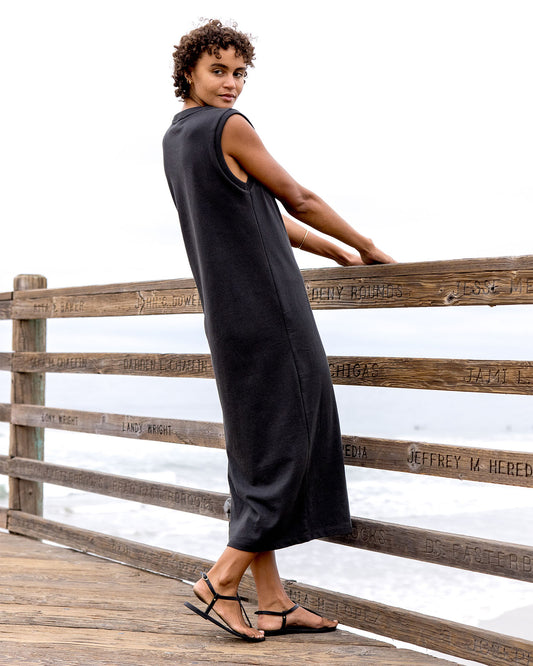 Woman in a black sleeveless dress standing on a wooden dock with a white background