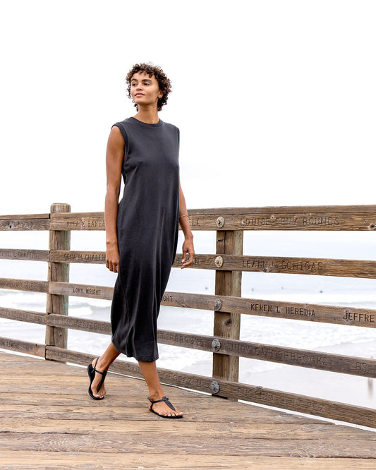 Woman in a black sleeveless dress standing on a wooden dock with a white background
