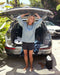 Person standing in front of an open car trunk with a surfboard, smiling.