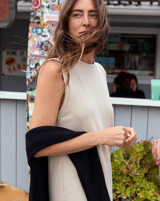 Woman wearing a sleeveless beige dress with a black arm cover, standing outdoors.