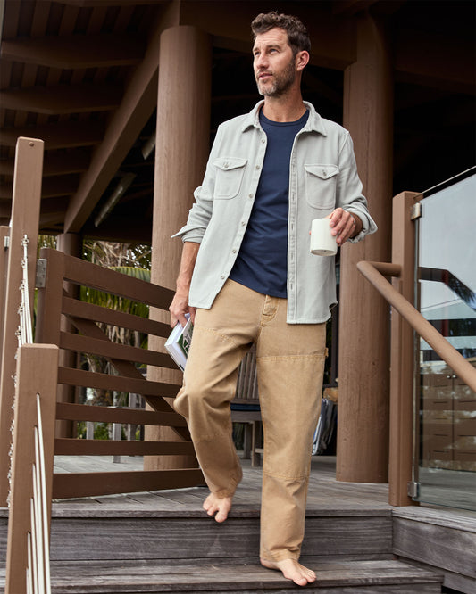 Man wearing a light gray blanket shirt standing on a wooden deck holding a coffee cup