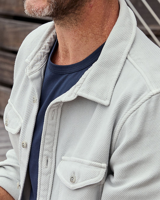 Man wearing a light gray blanket shirt over a dark blue shirt.