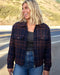 Woman wearing a plaid jacket standing on a road with a blurred background