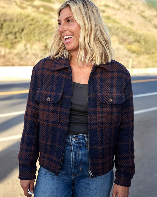 Woman wearing a plaid jacket standing on a road with a blurred background