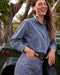 Woman in a blue corduroy outfit standing next to a green vehicle with trees in the background