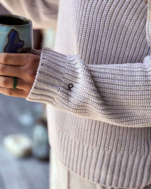 Person wearing a light gray knit sweater holding a ceramic mug with a blurred background