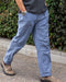 Person wearing blue pants and brown shoes standing against a green bush background