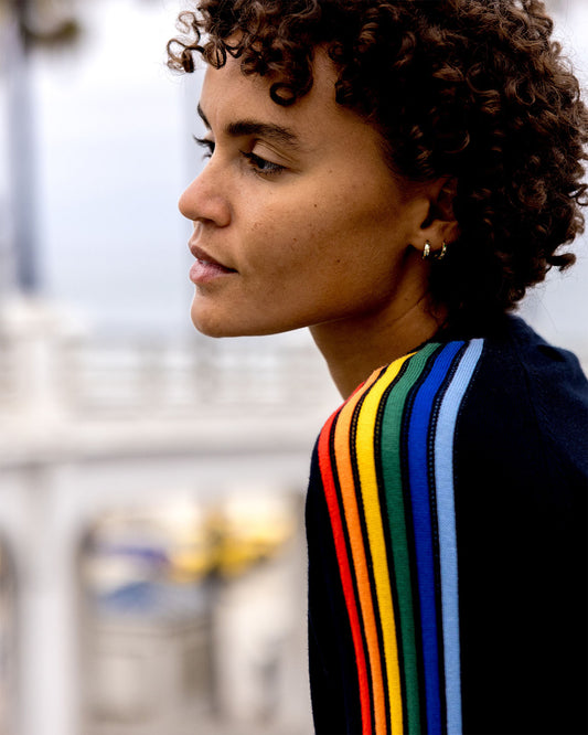 Person wearing a black jacket with rainbow stripes, standing outdoors.