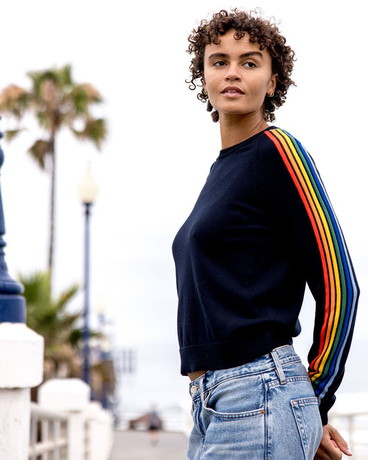 Person wearing a black sweater with rainbow sleeves outdoors