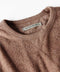 Close-up of a brown sweater with a brand label on a white background