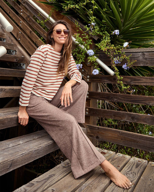 Woman sitting on wooden steps outdoors wearing a striped shirt and sunglasses.