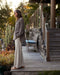 Woman standing on a wooden deck with plants and outdoor furniture in the background