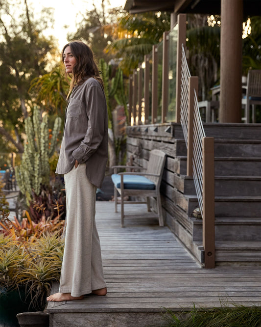 Woman standing on a wooden deck with plants and outdoor furniture in the background